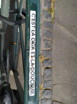 Mobilier urbain pour accrocher les vélos sur lequel est scotchée une bandelette de papier blanche, écriture noire majuscule C'est la cata et la douceur