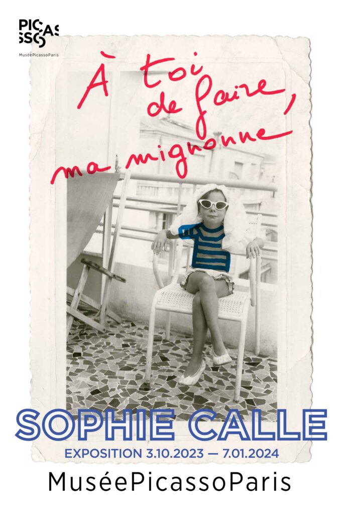 Affiche de l'exposition de Sophie Calle au musée Picasso qui a pour titre A toi de faire, ma mignonne. La photo est une photo de Sophie, enfant, assise sur une chaise avec des lunettes, une marinière dessinée sur la photo.